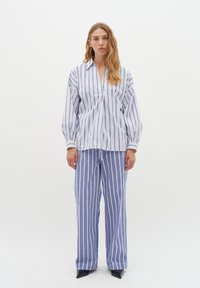 Set di pigiama a righe blu e bianche. La maglietta presenta un colletto e una vestibilità ampia; i pantaloni sono a gamba larga con righe verticali e una vita elastica.