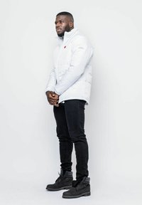 Vit puffjacka med hög krage, dragkedjestängning och röd logodetalj. Matchad med svarta skinny jeans och svarta stövlar.