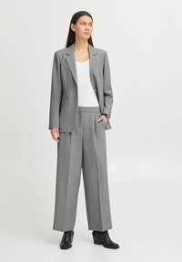 Grijze op maat gemaakte pak met een gestructureerde blazer en brede broekspijpen, met een subtiele krijtstreep en een zachte textuur. Zwarte hoge laarzen.