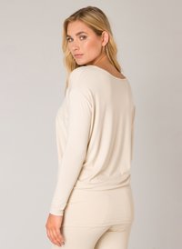 Beige langärmliges Oberteil mit lockerer Passform, rundem Ausschnitt und weichem Stoff. Mit drapiertem Rückendesign. Kombiniert mit passenden beigen Unterteilen.