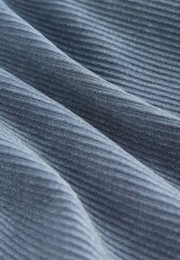 Blå ribbad tyg visar en mjuk textur med varierande nyanser. Ytan har fina vertikala linjer som framhäver dess taktila kvalitet.