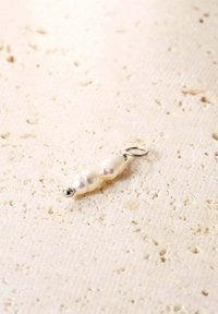 Pendentif en perles avec deux perles de couleur crème, texture lisse, quincaillerie couleur argent, et un petit accent rond en bas.