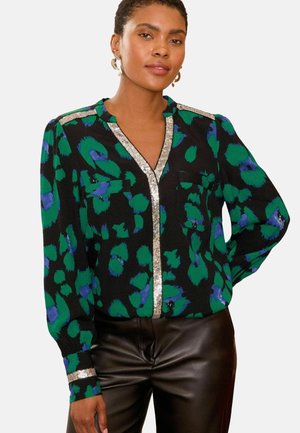 Schwarze Bluse mit grünem und blauem abstraktem Muster; mit silbernem Besatz entlang des Halsausschnitts und der Schultern; zwei Vordertaschen; lange Ärmel.