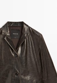 Bruine leren jas met een glanzende afwerking, schouderkraag, enkele knoopsluiting en een gladde binnenvoering. Het label leest "Massimo Dutti."