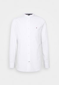 Camicia bianca a maniche lunghe con colletto a camicia, caratterizzata da chiusura con bottoni e un piccolo logo sul petto. Tessuto in cotone morbido.