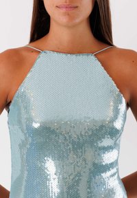 Top azzurro chiaro in paillettes con design a scollo all'americana, caratterizzato da una texture liscia e una superficie scintillante, che riflette la luce in varie angolazioni.