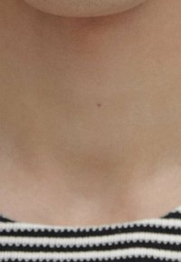 Un tessuto a righe bianche e nere con una texture liscia copre la zona superiore del petto, rivelando una piccola voglia sulla pelle sotto il decolletè.