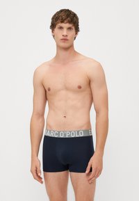Tengerészkék boxer alsónadrág szürke elasztikus derékpánttal, amelyen világosszürke betűkkel szerepel a "MARC O'POLO" márkaneve. Sima szövet textúra.