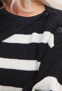 Sweter w czarno-białe paski o prążkowanej strukturze, z detalem w postaci guzika na ramieniu i szerokim dekoltem.