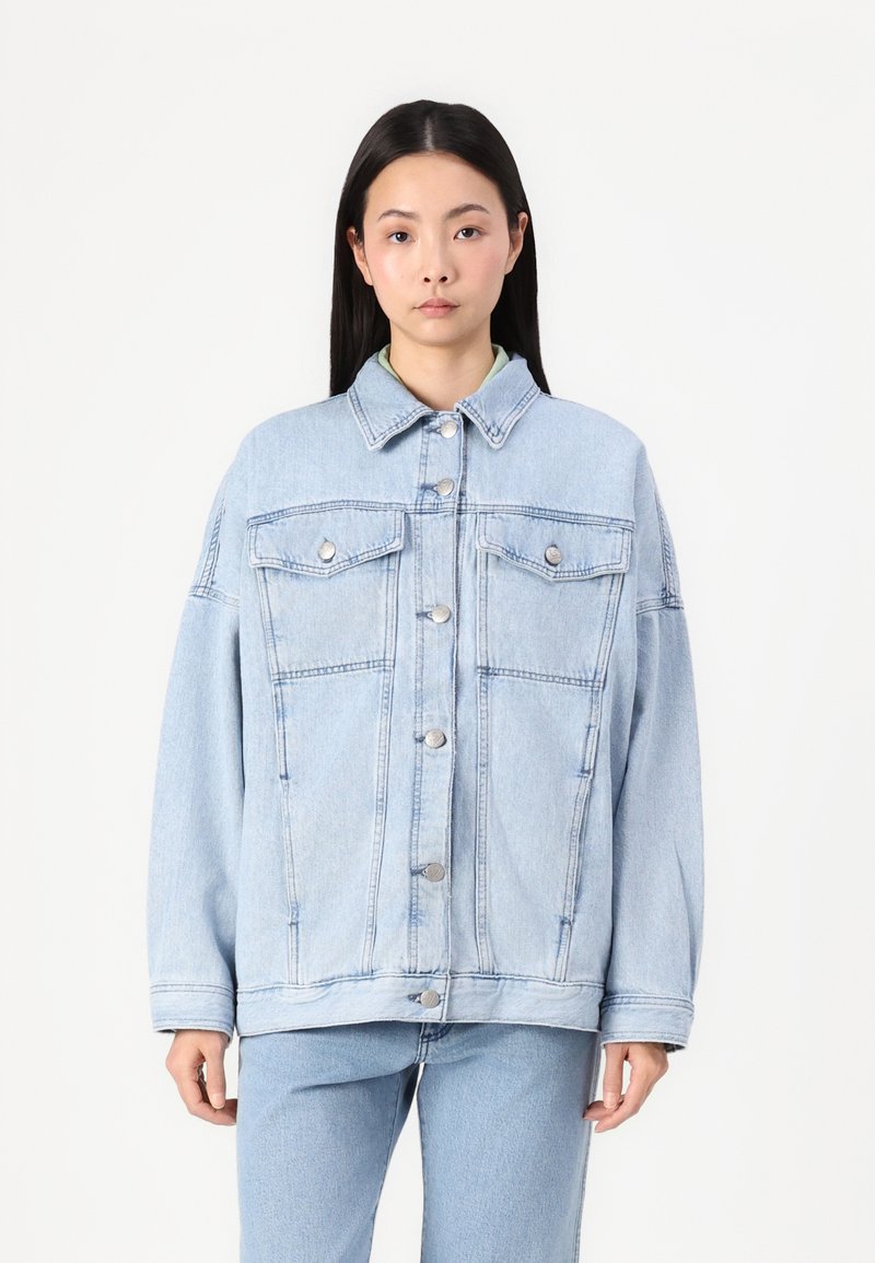 Lyseblå denimjakke med klassisk krage, frontknapplukning, to brystsjekker og en avslappet passform. Lange ermer og subtil falming.