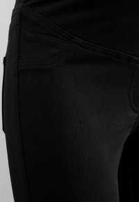 Gros plan sur un jean denim noir montrant une poche latérale et des coutures détaillées sur un vêtement ajusté.