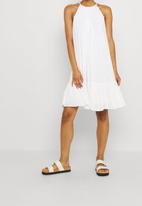 Bílý šaty se zavazováním za krkem, rozšířeným lemem, lehkou, splývavou látkou. Kombinované s bílými sandály s korkovou podrážkou.