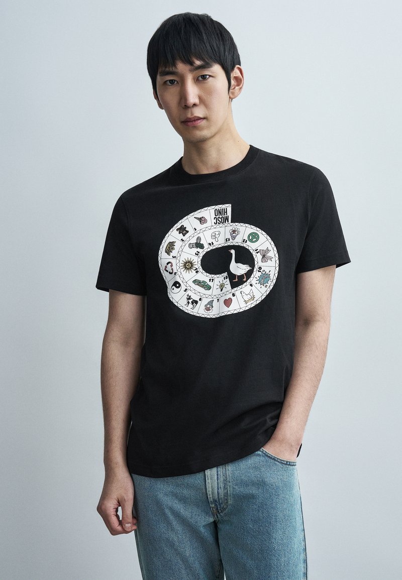 Μαύρο βαμβακερό μπλουζάκι με γραφικό τύπωμα ενός σπιράλ με διάφορα εικονίδια και κεντρικό σχέδιο χήνας. Συνδυάζεται με ανοιχτόχρωμο τζιν.