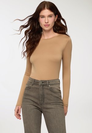 Maglietta a maniche lunghe color tan realizzata in un materiale liscio, abbinata a jeans a vita alta di un grigio scuro con cuciture sottili e tasche.
