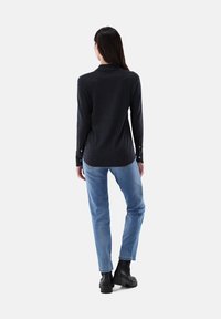 Dunkelgrau oberteil mit langen Ärmeln und Kragen, ausgestattet mit Knopfmanschetten. Kombiniert mit hellblauen Slim-Fit-Jeans und schwarzen Ankle-Boots.