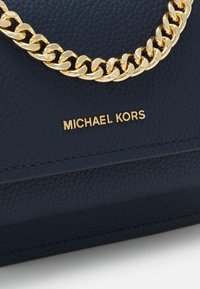 Námořnická kožená kabelka s zlatým řetízkovým akcentem a embosovaným logem. Obsahuje texturovaný materiál a strukturovaný tvar.