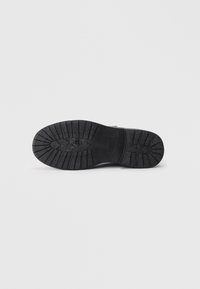 Rubber boot sole in black with a textured grip pattern. Features include a reinforced toe and decorative elements on the outsole.
