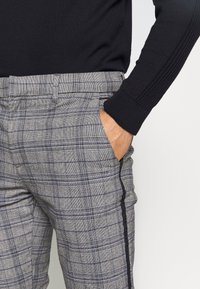 Grijze geruite trousers met een slim fit, zijstrookdetails, voorkruiszakken en een subtiele textuur. Gecombineerd met een zwart gebreid sweater.