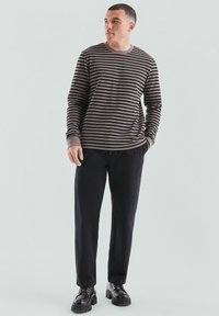 Gestreepte langesleeve shirt in donkerbruin en crème, gecombineerd met een zwarte broek en zwarte chunky laarzen. Beschikt over een ronde halslijn en opgerolde mouwen.