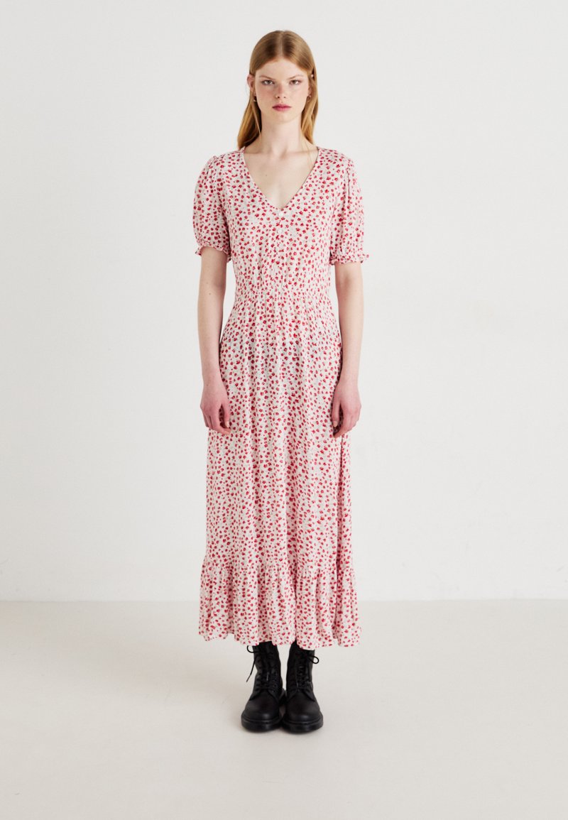 Rochie maxi din material ușor, cu imprimeu floral roșu, decolteu în V, mâneci bufante și tiv volanat. Asortată cu cizme negre cu șireturi.