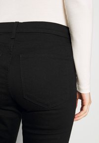 Jean noir au design ajusté, avec des poches arrière et des détails de couture. Le matériau semble en denim avec une texture lisse.