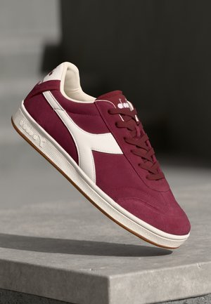 Baskets rétro bordeaux avec des accents blancs, design à lacets, en cuir suédé, semelle en caoutchouc texturée et logo de la marque bien en vue sur la languette.