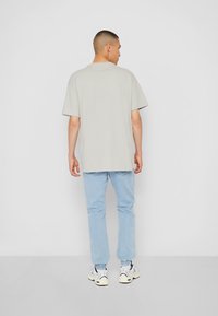 Tricou oversized gri deschis cu mâneci scurte, asociat cu blugi tapered bleu deschis și adidași albi. Design simplu, casual.