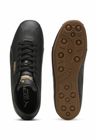 Czarne skórzane buty piłkarskie z teksturowanym wykończeniem, z złotymi akcentami i gumową podeszwą z okrągłymi punktami trakcyjnymi.