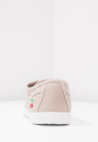 Scarpa slip-on in tela beige chiaro con suola in gomma bianca. Presenta ciliegie ricamate sul tallone e dettagli di cuciture testurizzate.