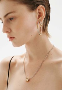 Joyas de oro y plata que incluyen un arete de aro grueso y texturizado, y un collar delicado con una cadena y un colgante circular.
