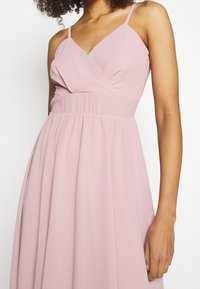 Světlé růžové bezramínkové šaty s výstřihem do V a nařaseným pasem. Vyrobené z měkké látky, s volánovou sukní a jemnými ramínky.
