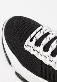 Baskets athlétiques noires avec tige en mesh texturé, lacets blancs et détails noirs contrastants. Présentent un col rembourré et une semelle intermédiaire blanche.