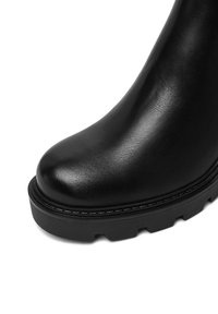 Melnas ādas potīšu zābaki ar noapaļotu purngalu, teksturētu virsmu un biezu gumijas zoli ar dziļām rievām, kas nodrošina saķeri.