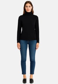 Schwarzer Rollkragenpullover aus weichem Strickmaterial, kombiniert mit figurbetonten blauen Jeans. Das Outfit zeigt eine schlichte, klare Silhouette.