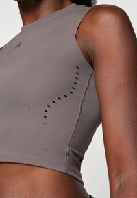 Sivi bezrukavi crop top s prilagođenim dizajnom, glatkom teksturom i perforiranim detaljem sa strane, izrađen od rastezljivog materijala koji upija vlagu.