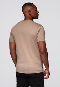 Beige lyhythihainen t-paita pyöreällä kaula-aukolla. Pehmeä kangas, kapea istuvuus, jossa pieni brändilogo helmassa. Takakatsaus esitetty.