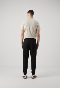 Camiseta de manga corta beige y pantalones jogger negros con puños elásticos. Los joggers tienen un bolsillo en la parte trasera. Zapatillas blancas con toques negros completan el conjunto.