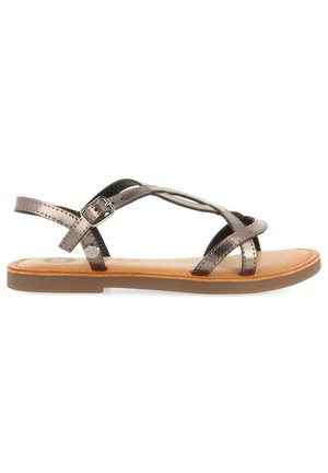Sandalias con tiras en bronce metálico, con correas entrecruzadas y un cierre lateral. Suela marrón antideslizante con plantilla beige suave.