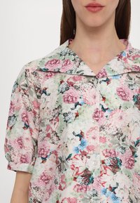 Floral blouse with short puff sleeves, featuring a pastel color palette of pink, green, and blue. Button-up front and wide collar design.