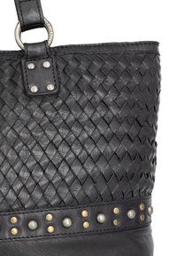 Czarna skórzana torba tote z plecioną powierzchnią, z ozdobną bandą nabijanymi ćwiekami w pobliżu podstawy oraz metalowym elementem w kształcie pierścienia na uchwycie.