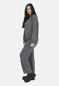 Maglione grigio lavorato a maglia con collo alto e maniche a coste, abbinato a pantaloni grigi a gamba larga. Indossato con stivali platform neri chunky.