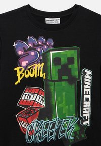 Czarna bawełniana koszulka z zielonym motywem Minecraft Creeper, czerwonymi blokami TNT oraz kolorowym napisem „Boom”, o kroju z okrągłym dekoltem.