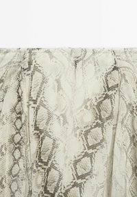 Gros plan d’un tissu beige avec un motif peau de serpent comprenant des formes en losange et des textures semblables à des écailles en tons gris et marron.
