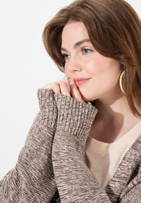 Hnědo melírovaný pletený cardigan s žebrovanými manžetami, texturovanou tkaninou a výstřihem do V, vrstvený přes krémovou košili.