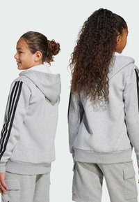 Ljust grå luvtröja med svarta ränder på ärmarna, tillverkad av mjukt material, med ribbat fåll och avslappnad passform.