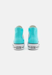 Light blue canvas high-top sneakers with white rubber soles, featuring a logo patch on the outer side and black stripes along the sole.