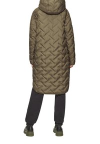 Lange olijfgroene pufferjas met een capuchon, met een chevron-gestikt patroon, tot halverwege de kuit, en elastische manchetten, gecombineerd met donkere broeken en laarzen.