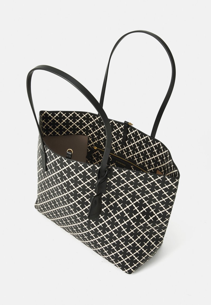 Svartvit mönstrad tygväska med två långa svarta handtag, som har ett rymligt inre och en blixtlåsficka för säker förvaring.