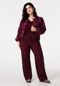 Bordeauxrode bomberjack met bloemenprint en opgepofte mouwen, gecombineerd met een bijpassende kanten top en wijde broekspijpen; puntige ballerina's met luipaardprint.