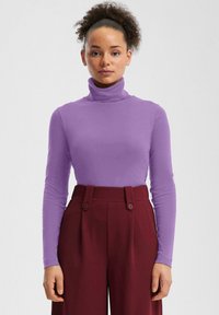 Top z długim rękawem i golfem w kolorze lawendowym, dopasowany krój, gładka tekstura. Połączony z wysokim stanem bordowych spodni z podwójnymi guzikami.
